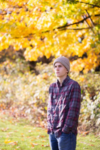 Pensive teen boy in toque and flannel shirt in front of yellow trees