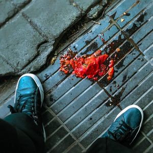 Low section of man standing by damaged tomato on sidewalk