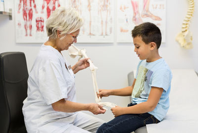 Senior female orthopedist showing hand model to boy at clinic