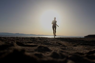 Silhouette woman running on beach against sky during sunset