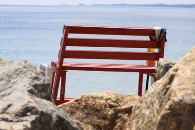 Red lifeguard chair on rock at beach against sky