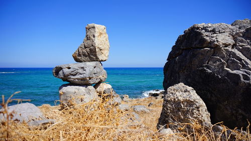 Rocks on sea shore against clear blue sky