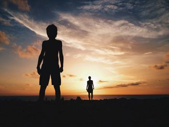 Silhouette people standing on landscape at sunset