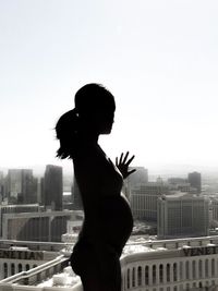 Full length of woman standing on balcony against cityscape