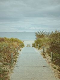 Footpath leading towards sea against sky