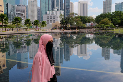 Reflection of woman on lake against buildings in city