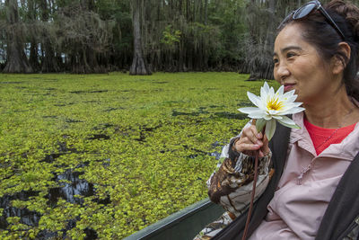 Smiling senior woman holding flower while sitting on boat