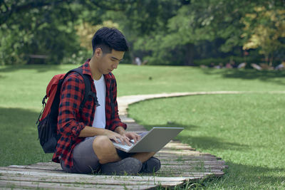 Young man using mobile phone while sitting on land