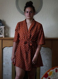 Portrait of teenage girl standing against wall at home