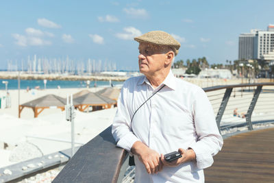 Senior man looking away while standing by railing on promenade