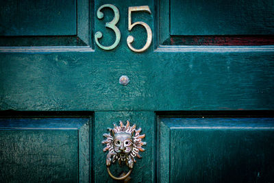 House number 35 with an exotic door knocker on a green wooden front door in london 