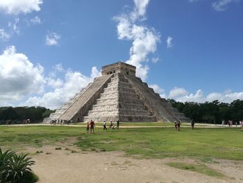 Tourists on field against cloudy sky