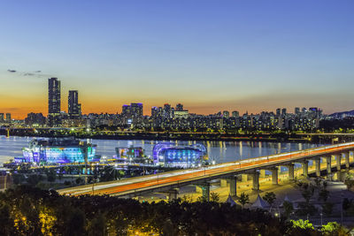 Illuminated bridge and buildings in city against clear sky during sunset