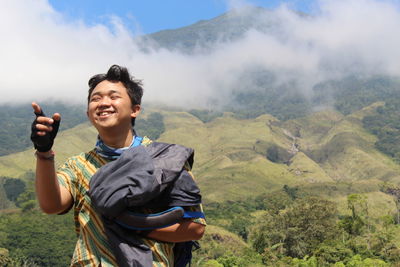 Smiling young man pointing while standing against mountains