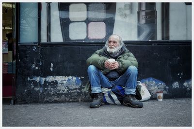 Full length portrait of man sitting in city