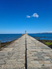 Footpath leading to sea against blue sky
