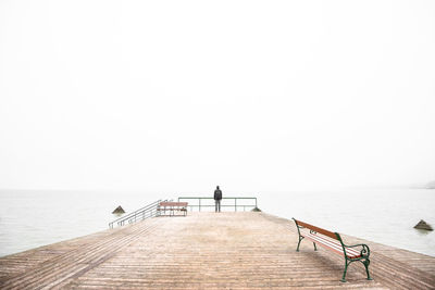 Man on pier against foggy sky