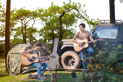 Friends playing guitars against vehicle on field