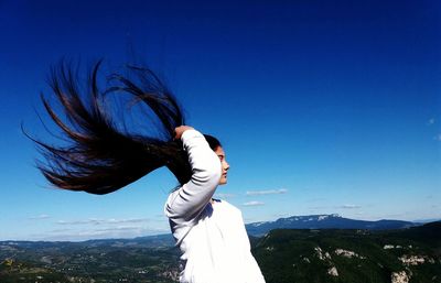 Young woman tossing hair against blue sky