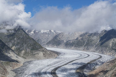 Snow covered road amidst mountains against cloudy sky