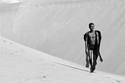 Full length of shirtless model with costume wing standing at desert