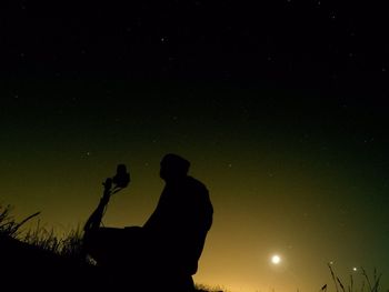 Low angle view of silhouette man with tripod at field against sky