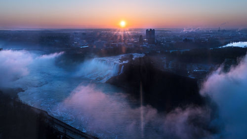Aerial view of city by sea against sky during sunset