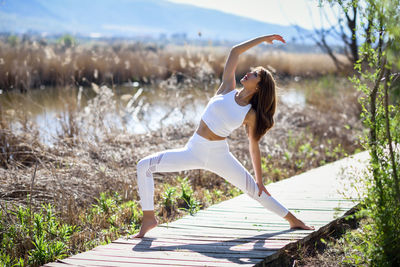 Beautiful mid adult woman doing yoga on boardwalk during sunny day