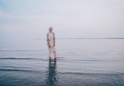 Woman wading in sea against sky