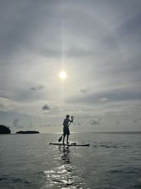 Rear view of man walking on beach against sky during sunset