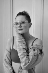 Portrait of young woman wearing sunglasses standing against wall