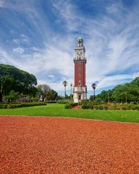 Lighthouse on field by building against sky