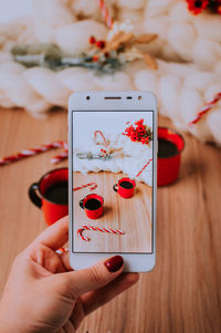 Close-up of hand photographing coffee cups on mobile phone at table