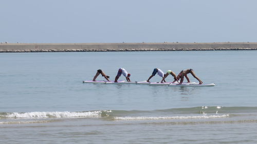 People exercising on paddleboard in sea against clear sky