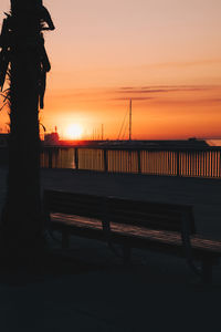 Silhouette statue on bench by sea against sky during sunset