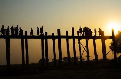 Silhouette people on bridge against sky during sunset