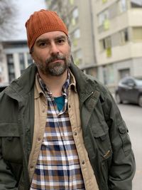 Pottarait of a bearded man wearing orange hat and green jacket standing outside 