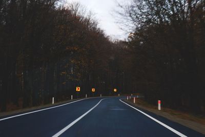 Empty road amidst trees against sky in city