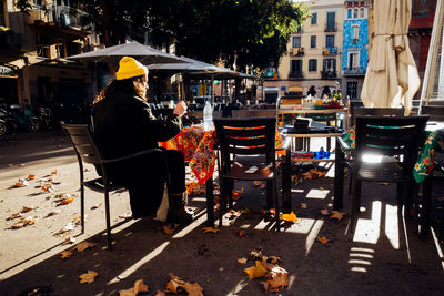 Rear view of man sitting on chair at sidewalk cafe