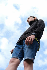 Teenager boy wearing black hoodie and shorts. low angle view. boy standing over a sky background. 