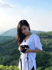 Beautiful young woman standing on mountain against sky