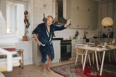 Senior man dancing while enjoying music through headphones in kitchen