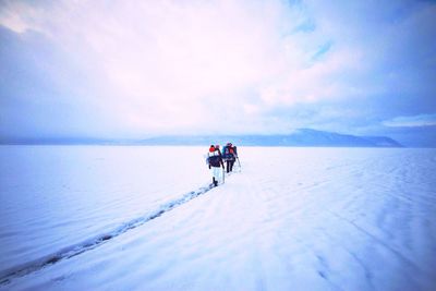 Rear view of hikers walking on snow covered field against cloudy sky