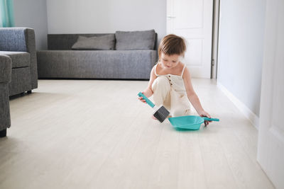 Cute european child with blue scoop and brush sweeping floor helps clean, development of montessori