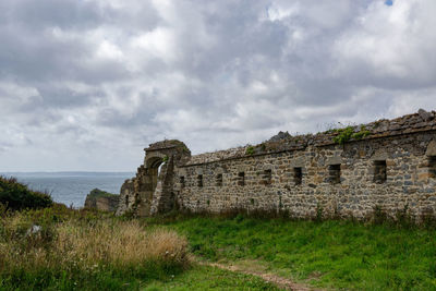 Old ruin on field by sea against sky