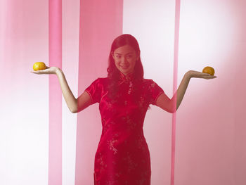 Portrait of smiling woman with oranges standing against backdrop