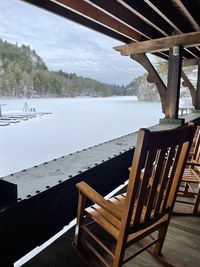 Empty chairs and table by lake against sky