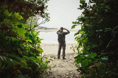 Rear view of man standing on a beach with green foliage