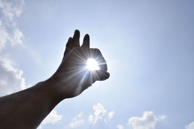 Low angle view of sun streaming through cropped hand