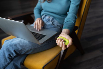 Woman working on laptop doing daily exercises with expander to strengthen fingers, hand and wrist